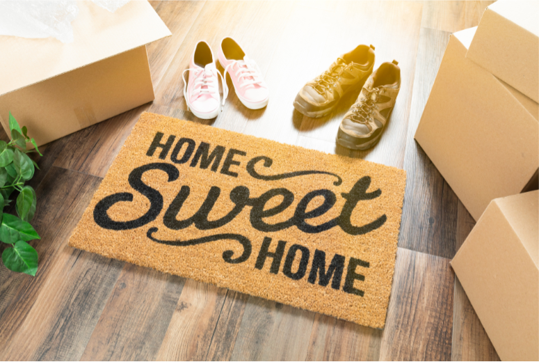 Doormat saying Home sweet home and 2 pairs of shoes on wooden floor