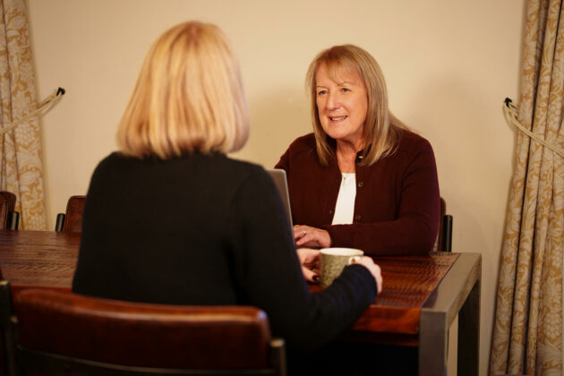Two women sat at a kitchen table in a home deep in conversation.