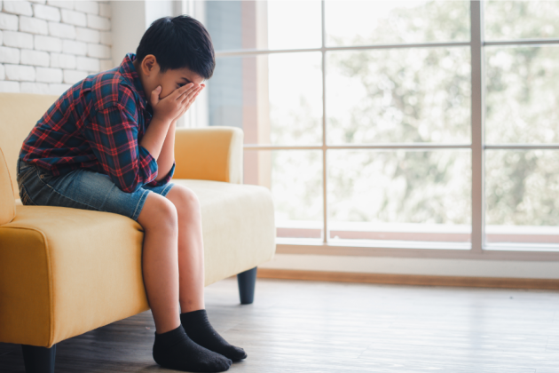 child sitting on sofa with hands covering face