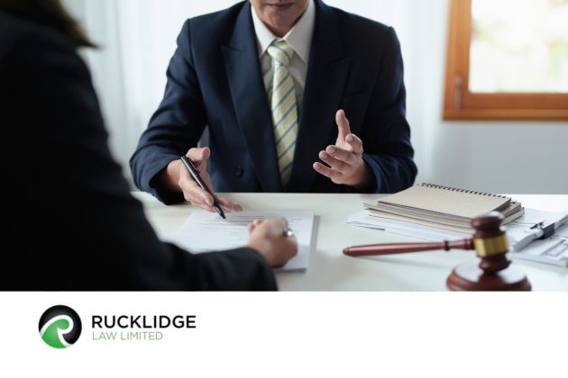 man in suit sitting at desk with back view of person in foreground looking at a document