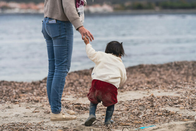 Woman walking along a beach holding hands with a small child.