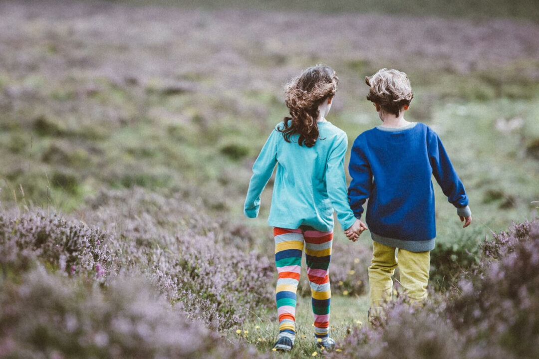 A young boy and girl holding hands and walking through a field of lavendar.