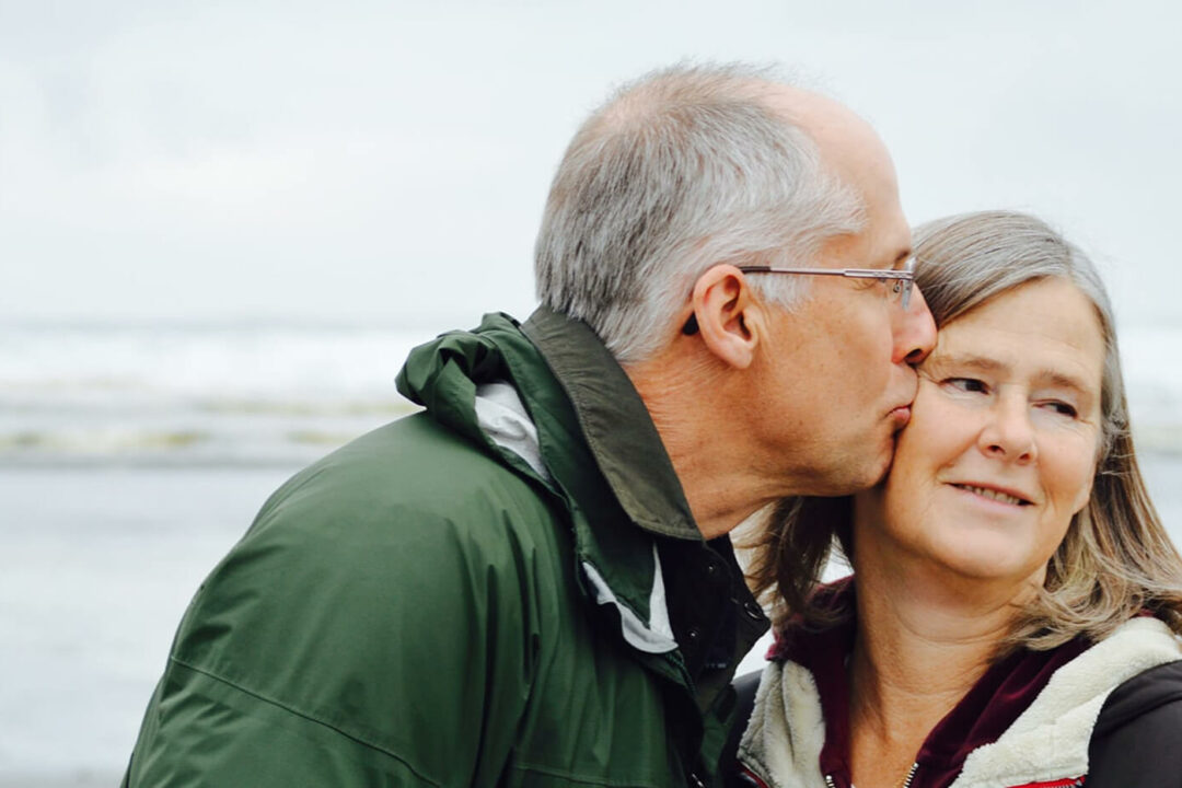 Elderly couple dressed for hiking embracing eachother on an overcast day.