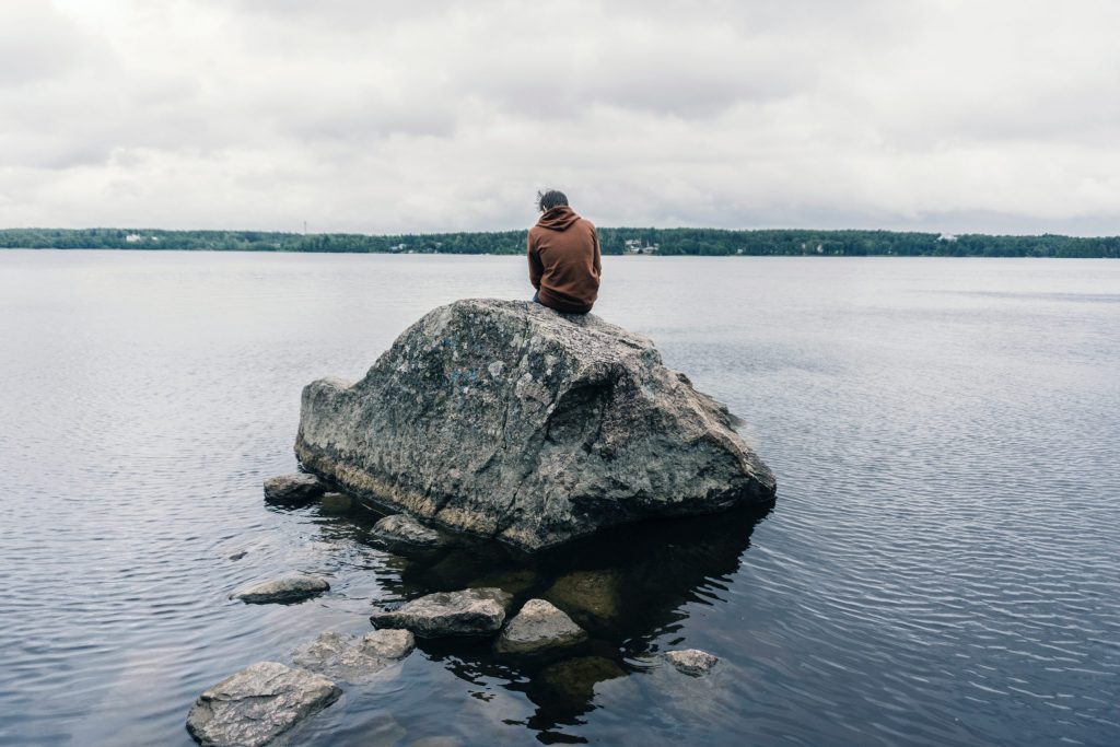 person sitting on large rock in water