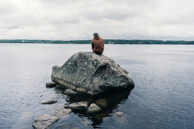 person sitting on large rock in water