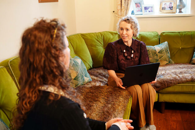 Solicitor sat in meeting in rustic house setting sat speaking to cleint on sofa.