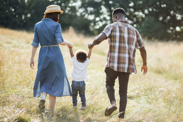 Two parents walking through a field holding hands with their child.