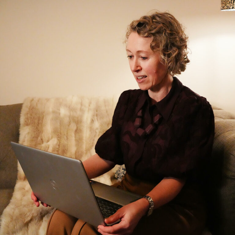 A solicitor sat in a comfortable lounge setting working from home, speaking to a client online.